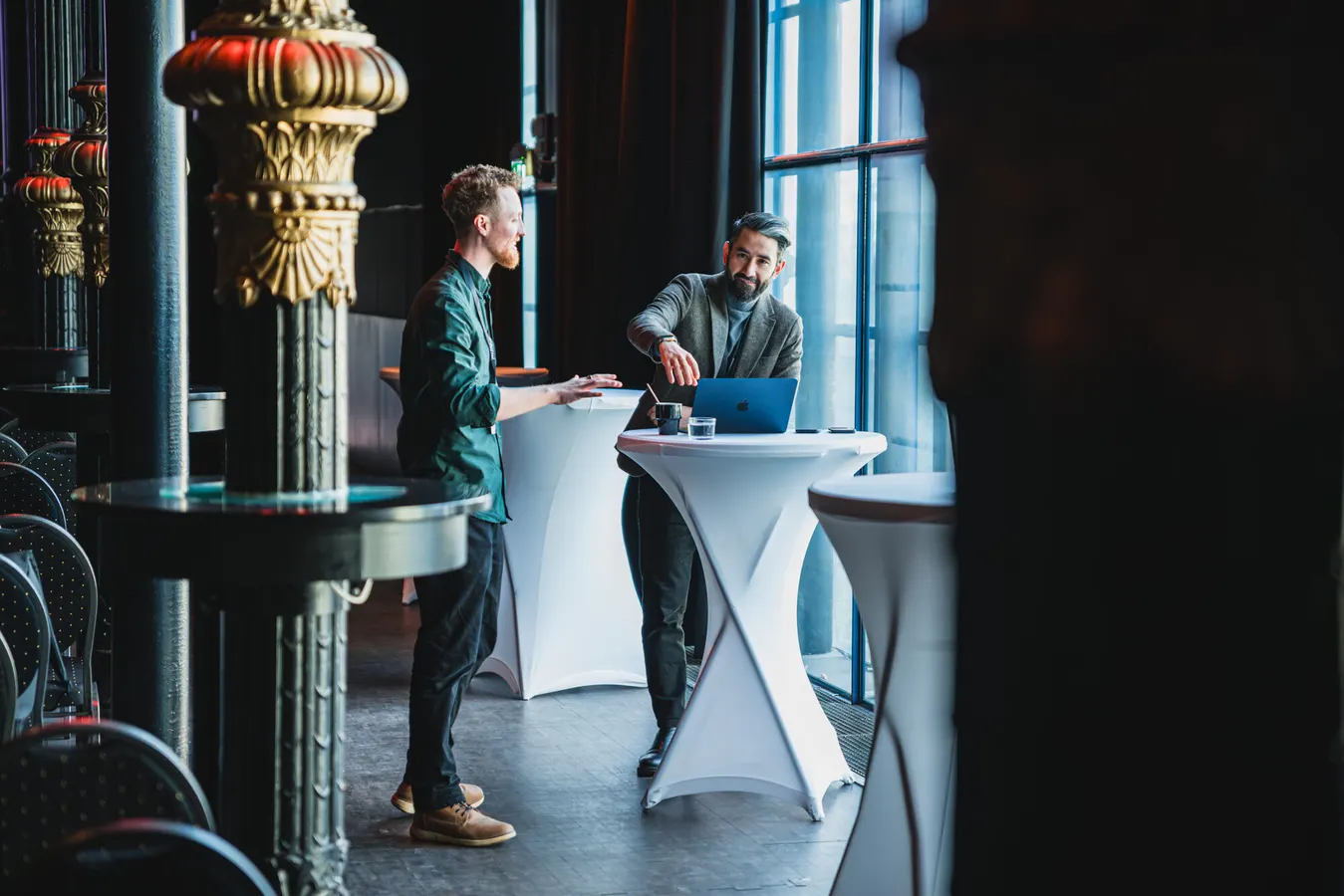 Two men talking at a standing table by a window
