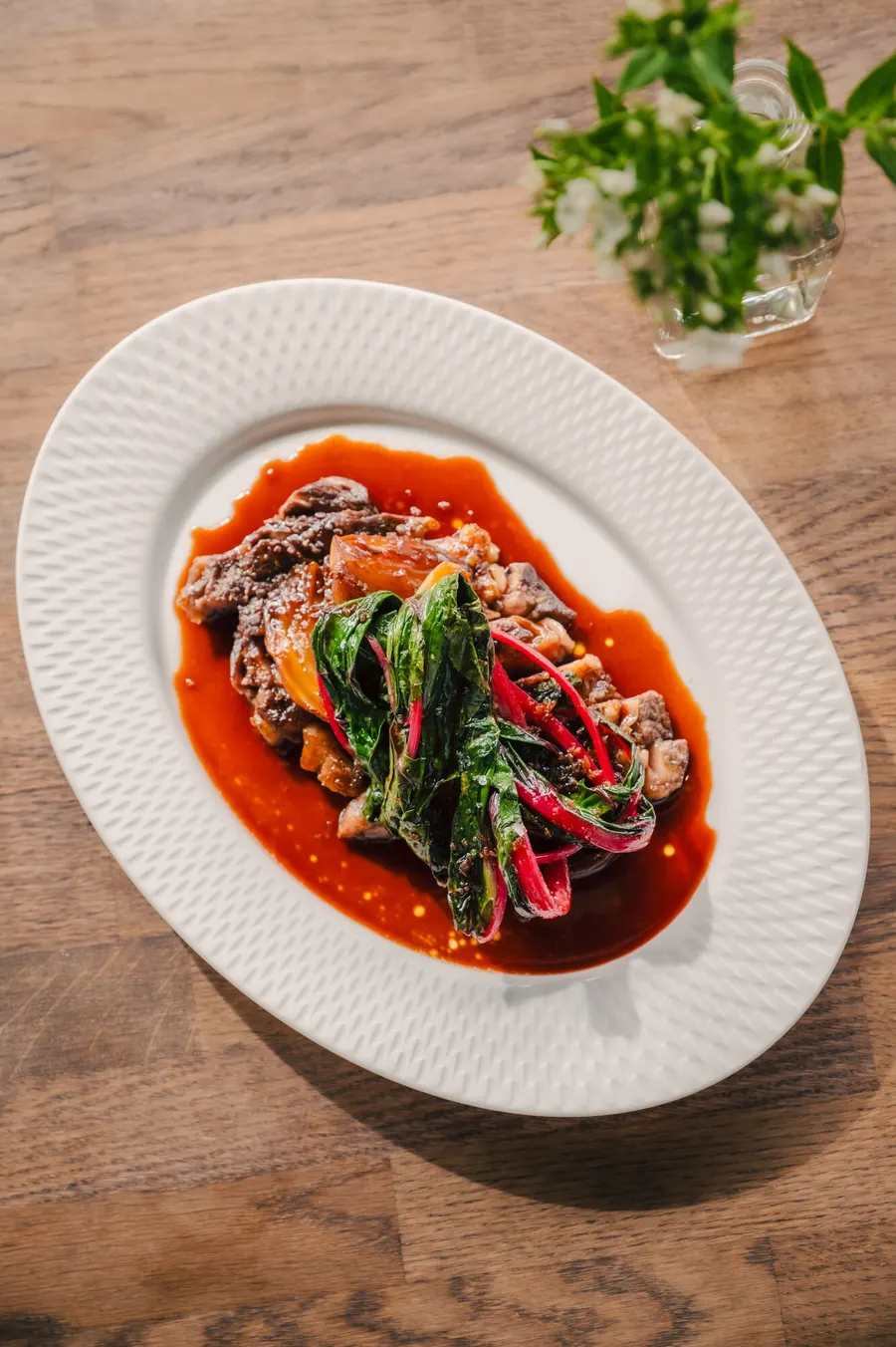 Short rib with chard in red sauce on an oval plate