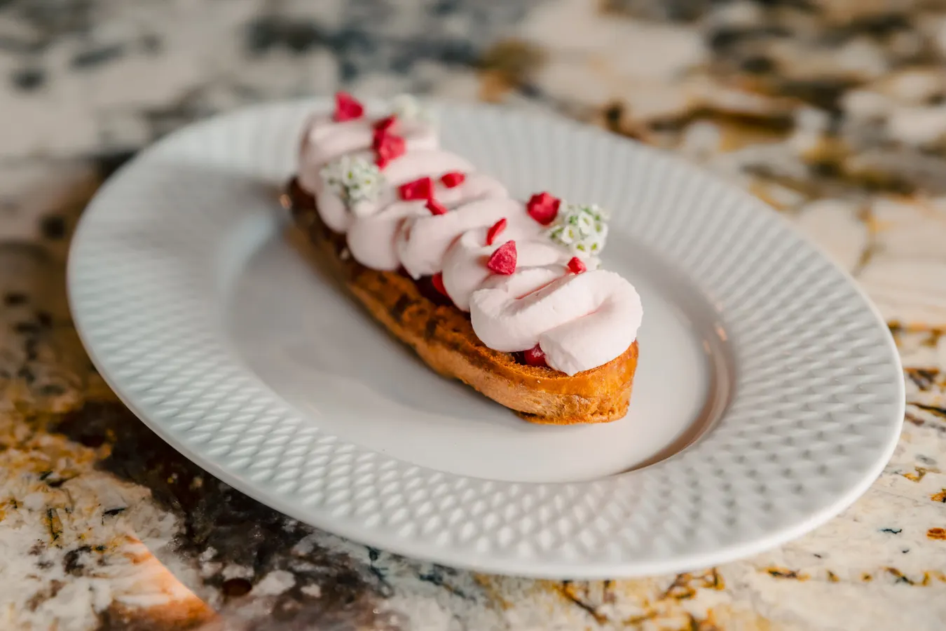 Éclair topped with pink cream and raspberries
