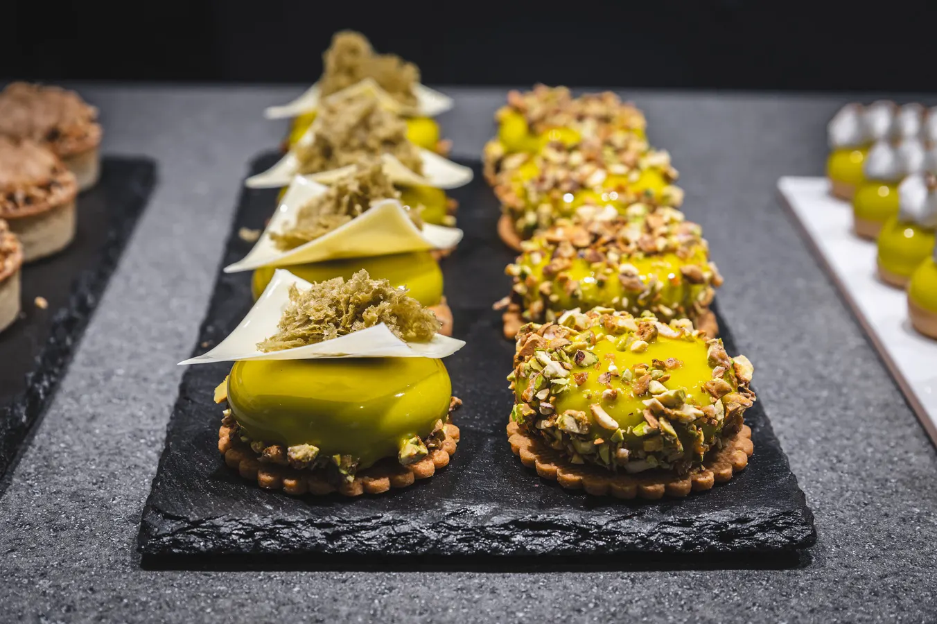 Rows of pistachio and lemon tarts on slate